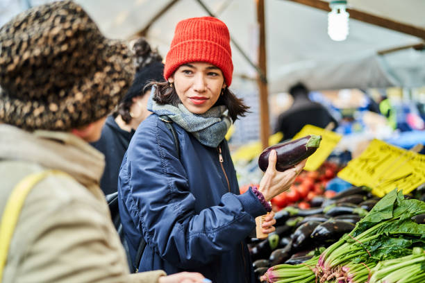Young woman holding a vegetable and talking with female friend in market. Female friends buying vegetables at local market in the city.